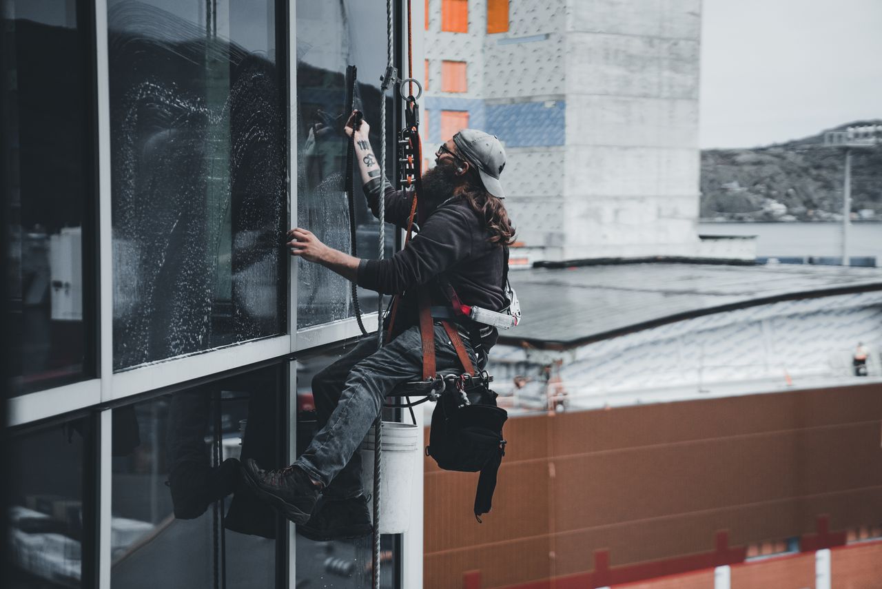 our-story A man cleaning skyscraper windows with a harness, showcasing urban high-rise work.