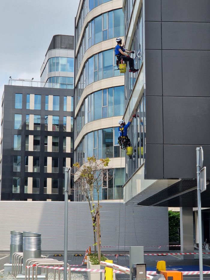 creative-01 Two workers clean windows on a tall office building in a city setting.
