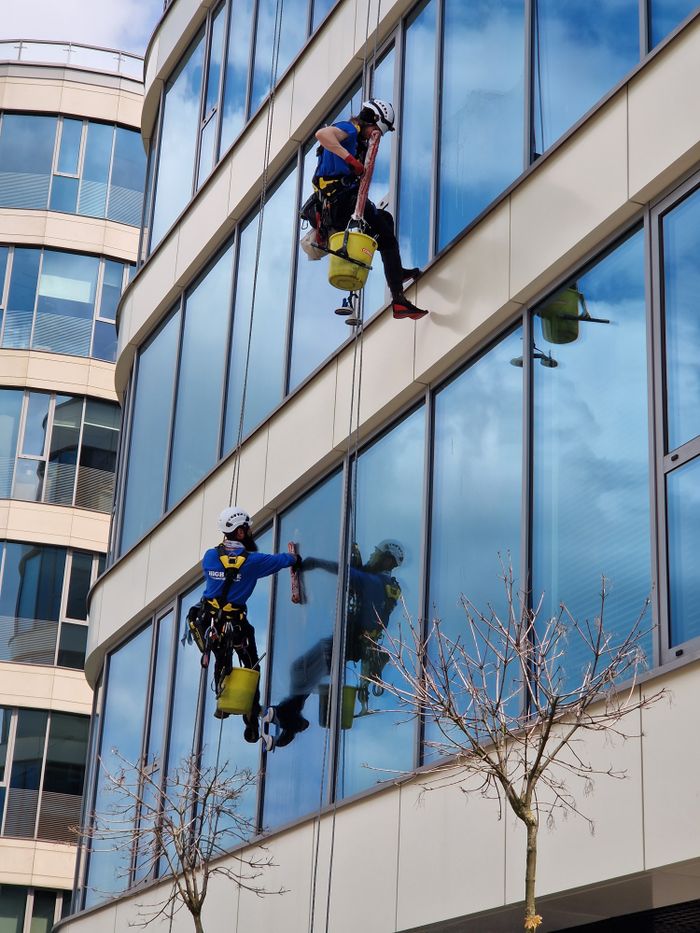 creative-03 Two window cleaners using ropes on a modern skyscraper, showcasing urban professional maintenance.